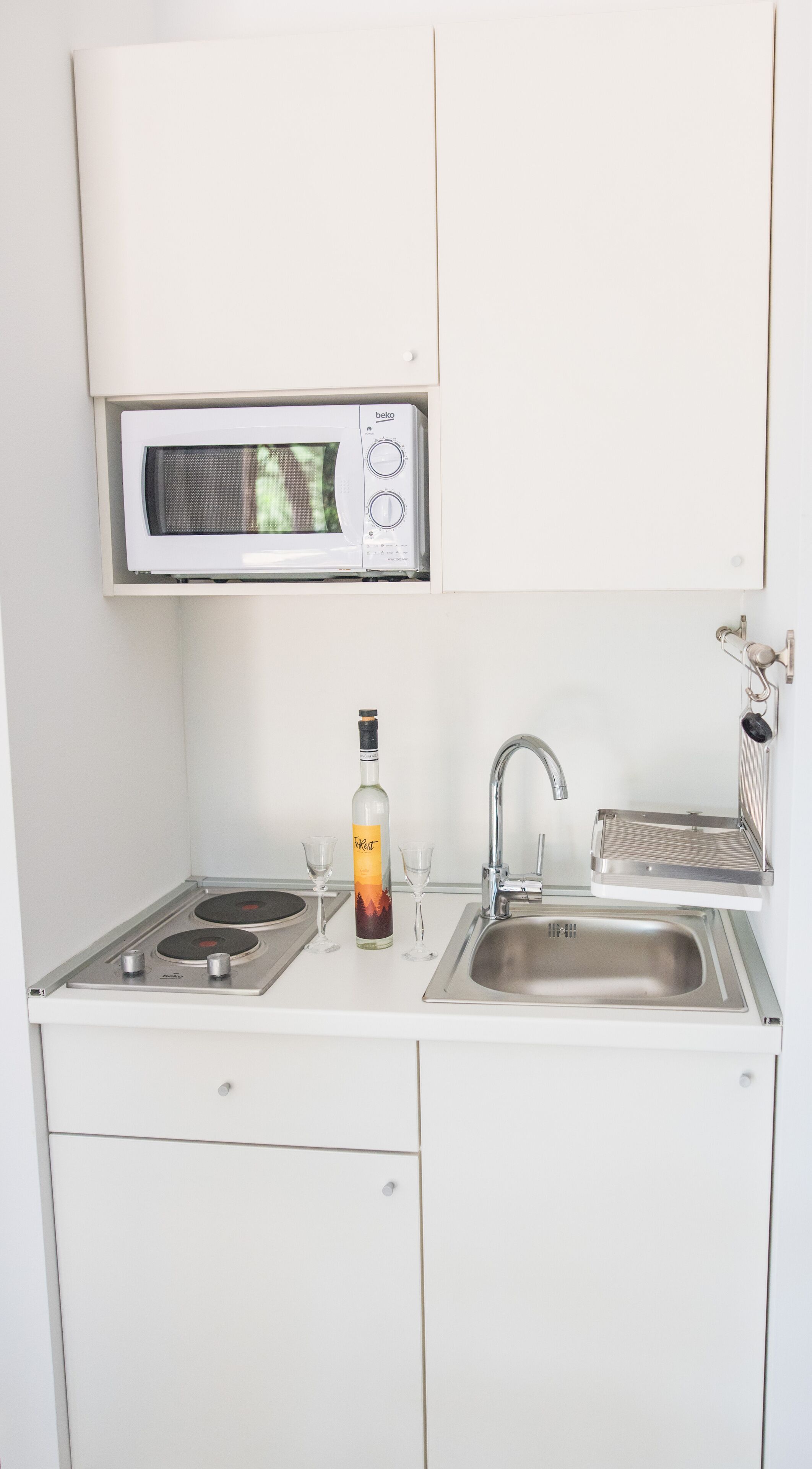 Een kleine keuken met een magnetron, gootsteen en een fles drank.