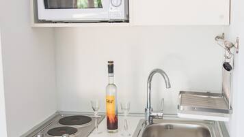 Een kleine keuken met een magnetron, gootsteen en een fles drank.