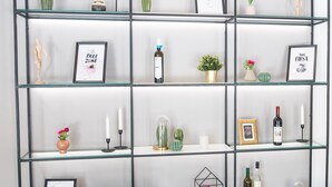 Un interior moderno con una estantería de vidrio y metal que exhibe diversos objetos decorativos, como cuadros enmarcados, velas y pequeñas plantas.