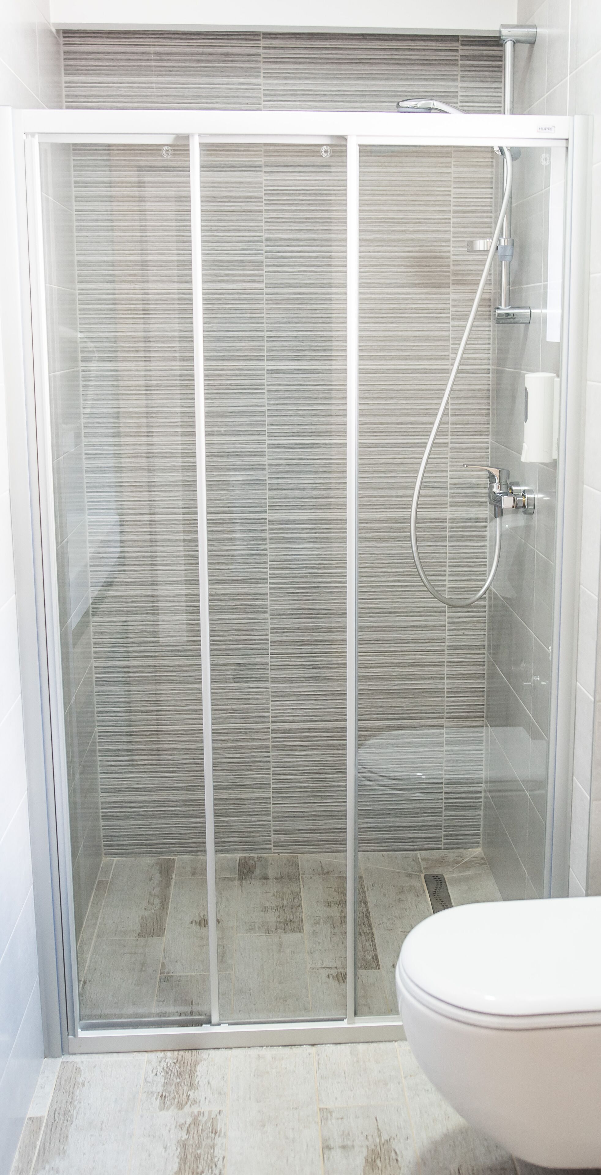 A modern bathroom with a glass-enclosed shower, a toilet, and a tiled floor.