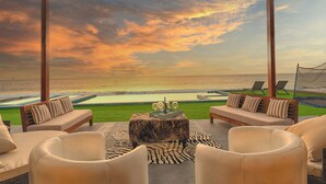 A terrace with a view of the ocean, featuring a wooden pergola, seating area with cushions, and a small table with a decorative centerpiece.