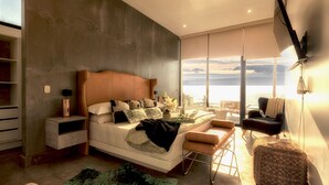 A modern bedroom with a large bed, a view of the sea, and a balcony.