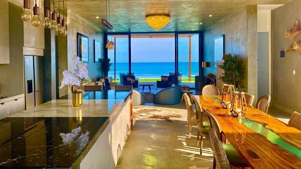 A modern interior with a large dining area, a kitchen, and a view of the ocean.