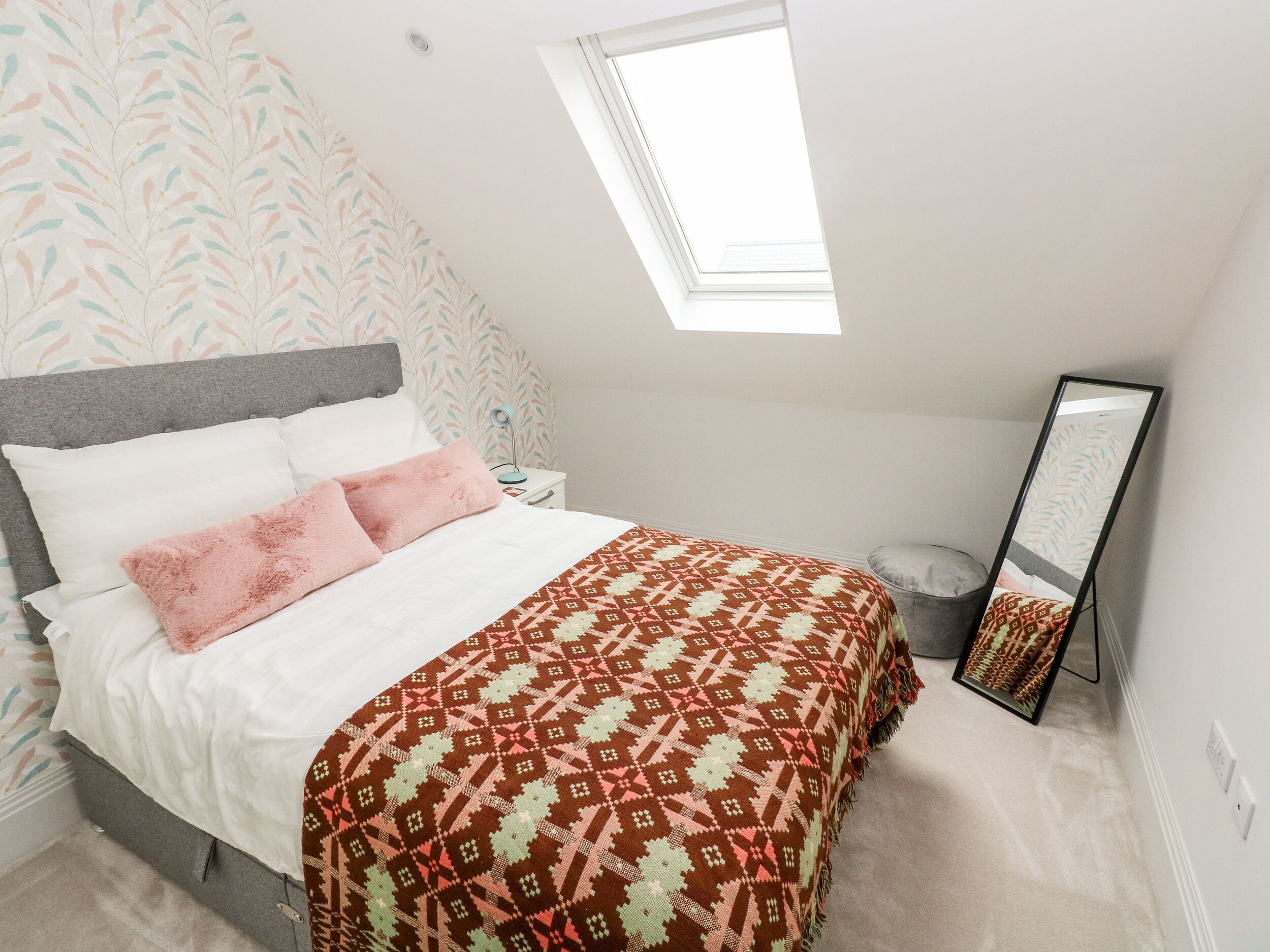 Un dormitorio con cama, mesita de noche, espejo y tragaluz.