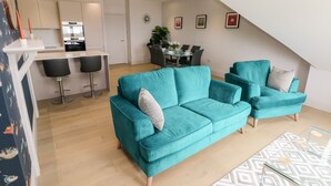 Una sala moderna con sofás color turquesa, un comedor y una cocina.