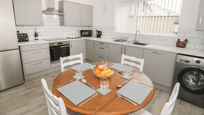Una cocina moderna con armarios blancos, una mesa redonda de madera y una lavadora integrada.