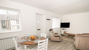 Una sala de estar moderna con comedor, muebles blancos, un televisor de pantalla plana y vistas al exterior.
