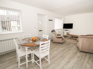 Un salon moderne comprenant un coin repas, un canapé et un téléviseur fixé au mur.