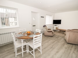 Una sala de estar moderna con comedor, muebles blancos, un televisor de pantalla plana y vistas al exterior.