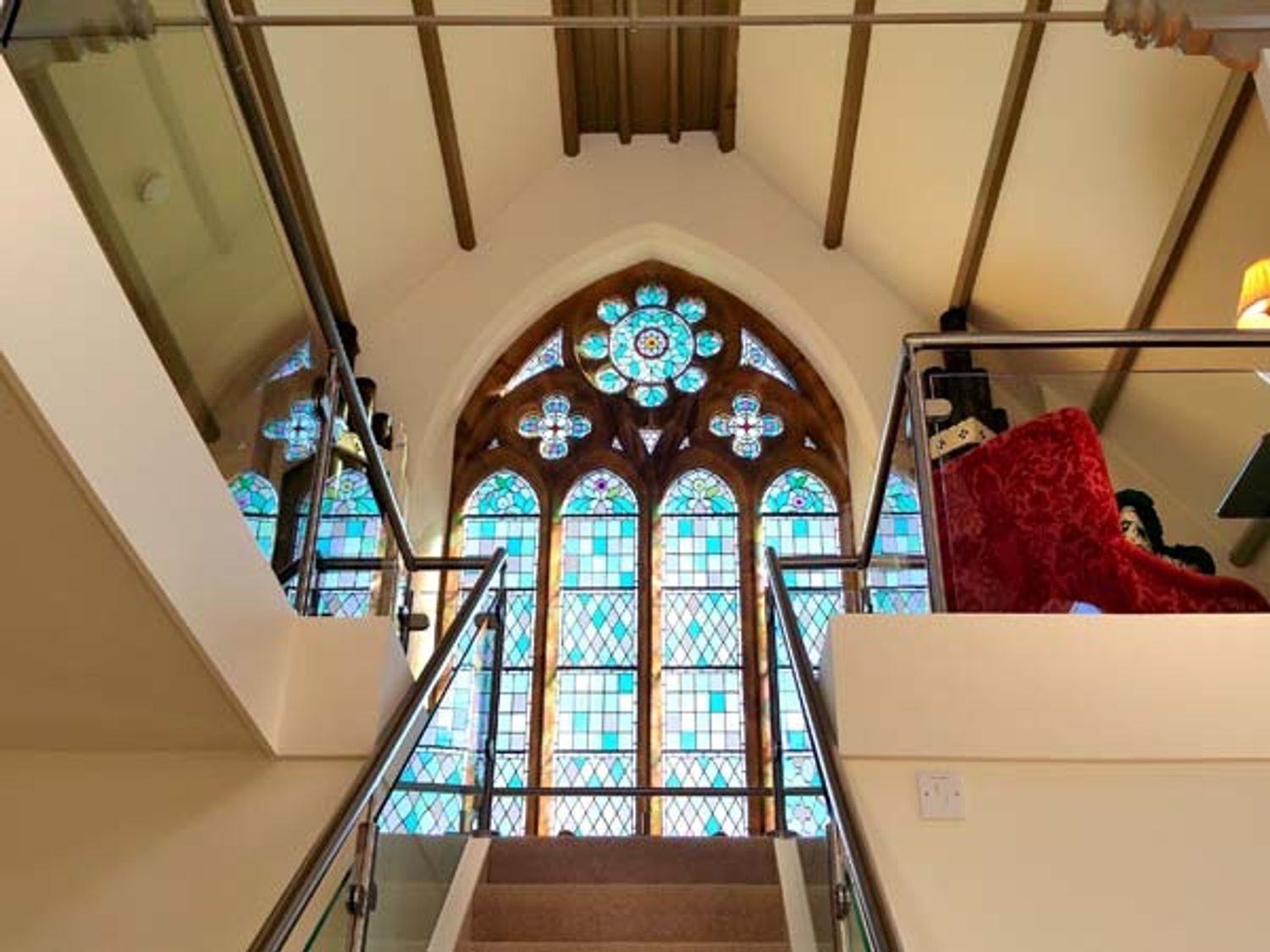 A staircase leading to a stained glass window with a cross design, surrounded by wooden beams and a glass railing.