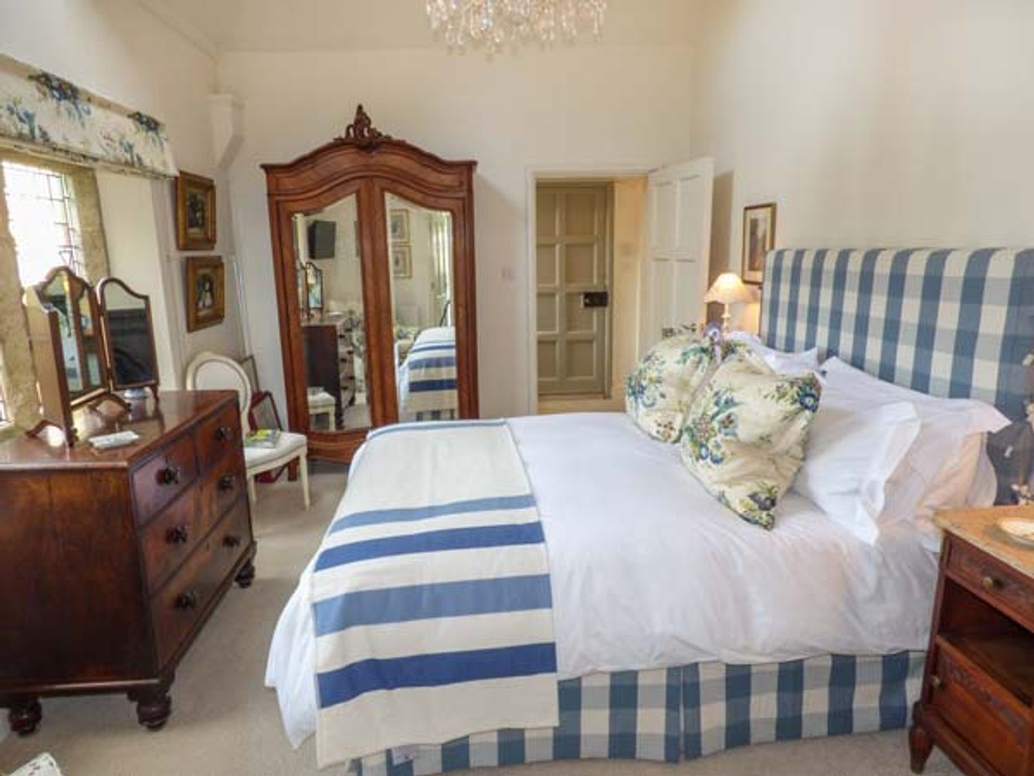 A bedroom with a bed, dresser, mirror, and a door leading to another room.