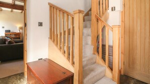 A staircase with wooden railings leading to a landing, a closed wooden door, and a small wooden table in a room with a carpeted floor. - The Priory (Bakewell)