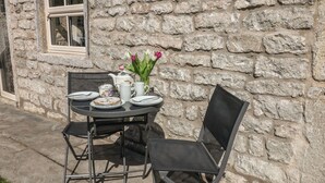 An outdoor dining setup with a stone wall backdrop, a table with chairs, and a vase of flowers. - The Priory (Bakewell)