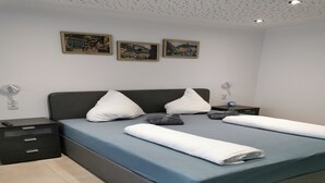 Un lit bien fait, avec un matelas bleu et du linge de lit blanc, une tête de lit sombre et trois tableaux encadrés accrochés au mur.