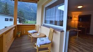 Un balcon avec des meubles en bois, une fenêtre avec des rideaux et une vue sur les montagnes.