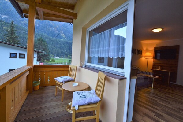 A balcony with wooden furniture, a window with curtains, and a view of mountains. - Apartment in Oetz near Ski Lift (Oetz)