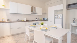 Una cocina moderna con armarios blancos, una mesa de comedor con platos amarillos y un refrigerador con imanes.