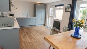 A modern kitchen with grey cabinets, a wooden dining table, and a blue vase with flowers. - 3 St. Cuthberts Garth (Bamburgh)