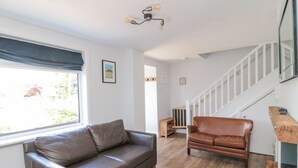 A living room with a brown leather sofa, a wooden bench, and a staircase. - 3 St. Cuthberts Garth (Bamburgh)