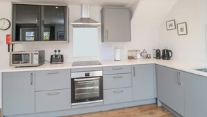 A modern kitchen with grey cabinets, a built-in microwave, a toaster, a kettle, and a coffee maker on the counter. - 3 St. Cuthberts Garth (Bamburgh)