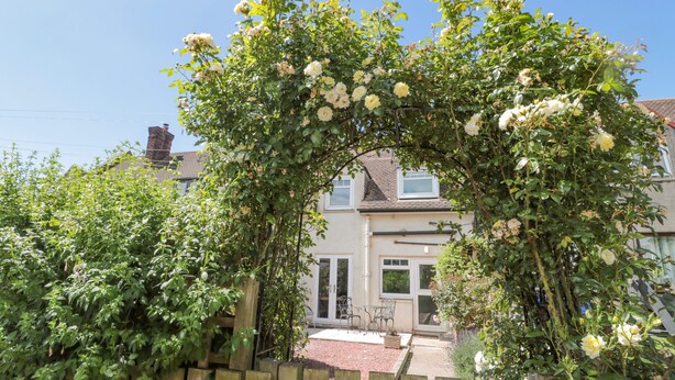 A wooden fence with the number 3, a garden with roses, and a house with a tiled roof in the background. - 3 St. Cuthberts Garth (Bamburgh)