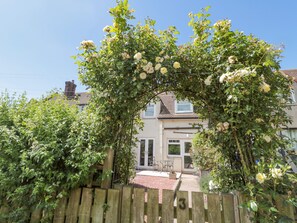 A wooden fence with the number 3, a garden with roses, and a house with a tiled roof in the background. - 3 St. Cuthberts Garth (Bamburgh)