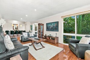 Ein modernes Wohnzimmer mit Ledersofas, einem Holztisch und einem großen Fenster mit Blick auf Grünflächen.