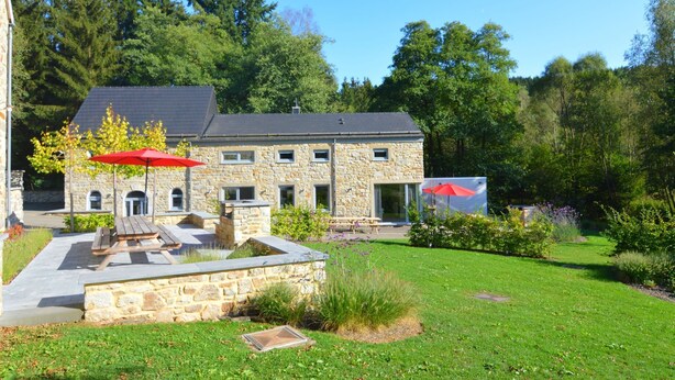 Una casa de piedra con un patio, un paraguas rojo y un jardín.
