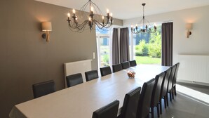 Un comedor moderno con una mesa larga, sillas negras, candelabros y vistas a la vegetación exterior.
