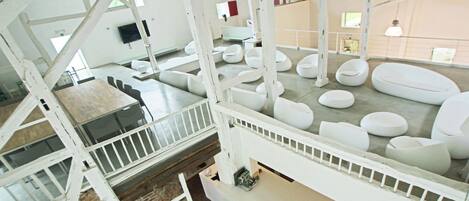 A spacious interior with a high ceiling, white structural beams, and multiple seating areas with modern, circular chairs.