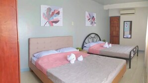 Camera d'albergo con due letti, ognuno dotato di poggiatesta, cuscini e asciugamani. Si notano due opere d'arte appese al muro, una porta e un condizionatore d'aria.