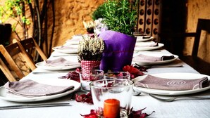 Una mesa dispuesta con platos, vasos y una vela, rodeada de plantas decorativas y hojas rojas.