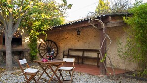 Un área de estar al aire libre con una mesa y sillas, una gran rueda de madera y un edificio rústico con techo de tejas.