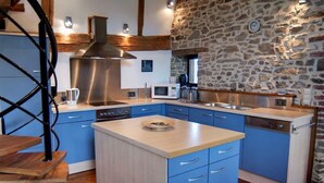 A modern kitchen with blue cabinets, a central island, stainless steel appliances, and exposed wooden beams. - Holiday Home in Verviers with Sauna & Fireplace (Ensival)