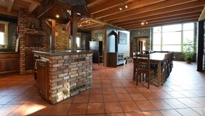 A spacious kitchen with a stone fireplace, wooden ceiling beams, and a large dining table. - Renovated Mill in Bastogne near Waterfall (Bastogne)