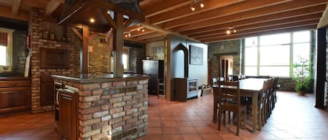 A spacious kitchen with a stone fireplace, wooden ceiling beams, and a large dining table.