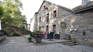 A stone building with a gravel courtyard, outdoor seating, and potted plants. - Renovated Mill in Bastogne near Waterfall (Bastogne)