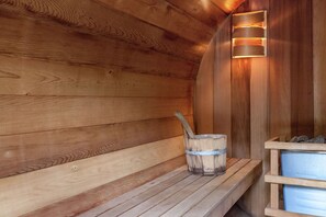 A wooden sauna with benches, a bucket, and a wall-mounted light fixture. - Holiday Home in Saint-Hubert with Sauna (Saint-Hubert)