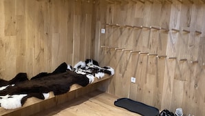 A wooden room with a fur-covered bench, a black mat, and a wall-mounted rack with hooks.