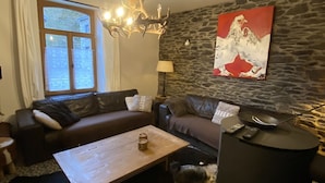 A living room with a stone wall, a chandelier, a painting, a sofa, a coffee table, and a dog.