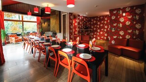 Un comedor con mesas rojas y negras, sillas anaranjadas y lámparas colgantes rojas.