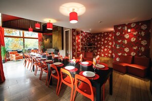 Un comedor con mesas rojas y negras, sillas anaranjadas y lámparas colgantes rojas.