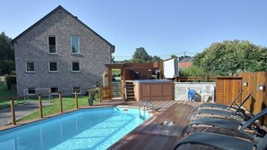 A swimming pool with a wooden deck and lounge chairs, a hot tub, and a brick building in the background. - Holiday Home in Stoumont near Coo Waterfalls (Rahier)