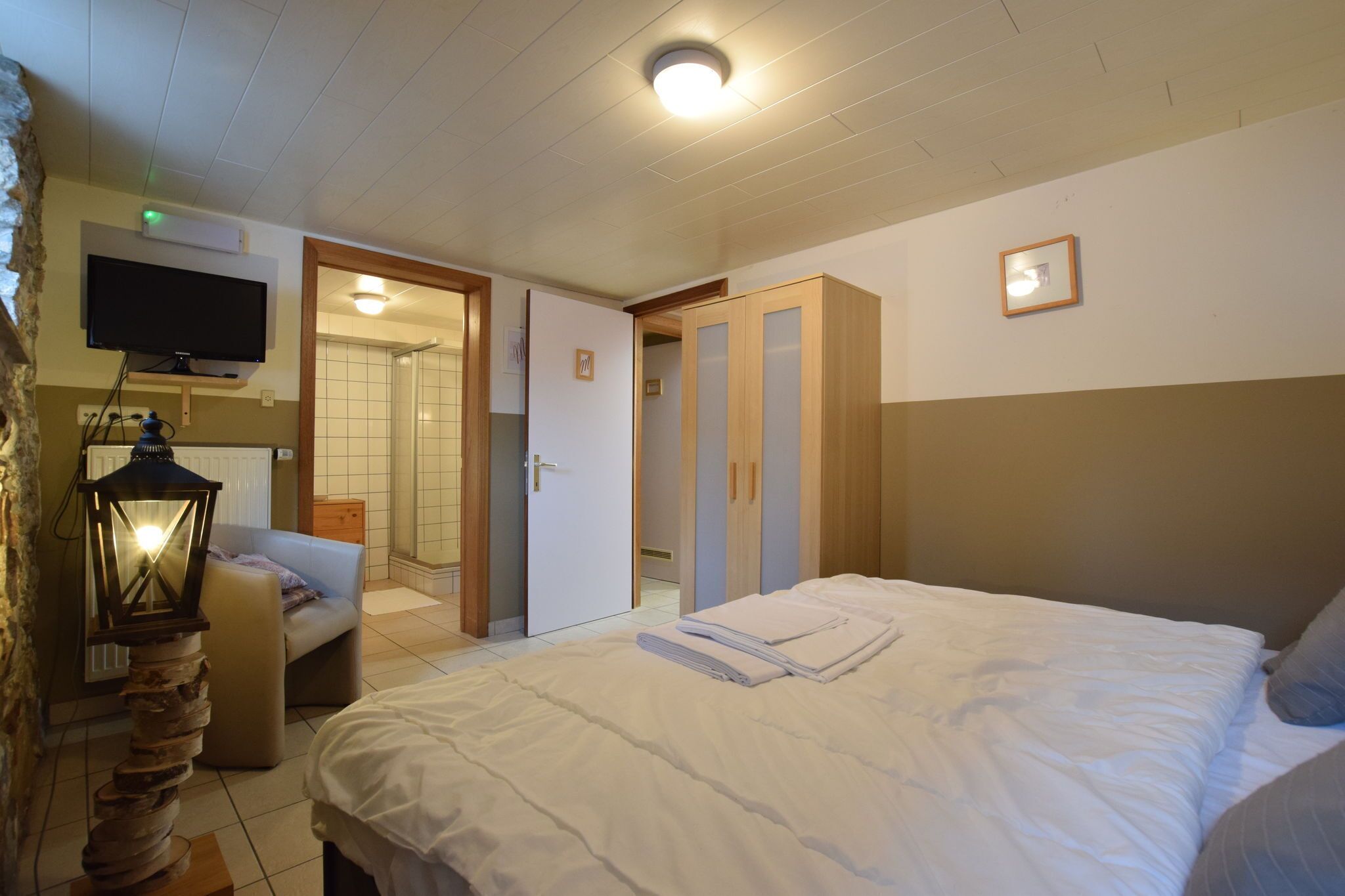 A hotel room with a bed, a television mounted on the wall, a wardrobe, and a bathroom visible through an open door.