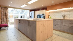 A modern kitchen with wooden cabinets, a central island, and a large window. - Holiday Home in Ardennes with Sauna & Pool (Vielsalm)