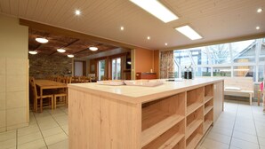 A spacious kitchen with a wooden island, a dining area with chairs, and a stone accent wall. - Holiday Home in Ardennes with Sauna & Pool (Vielsalm)