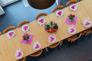 A long wooden dining table set for a meal with pink napkins, white plates, and a fruit centerpiece. - Comfy home near the forest with sauna (Waimes)
