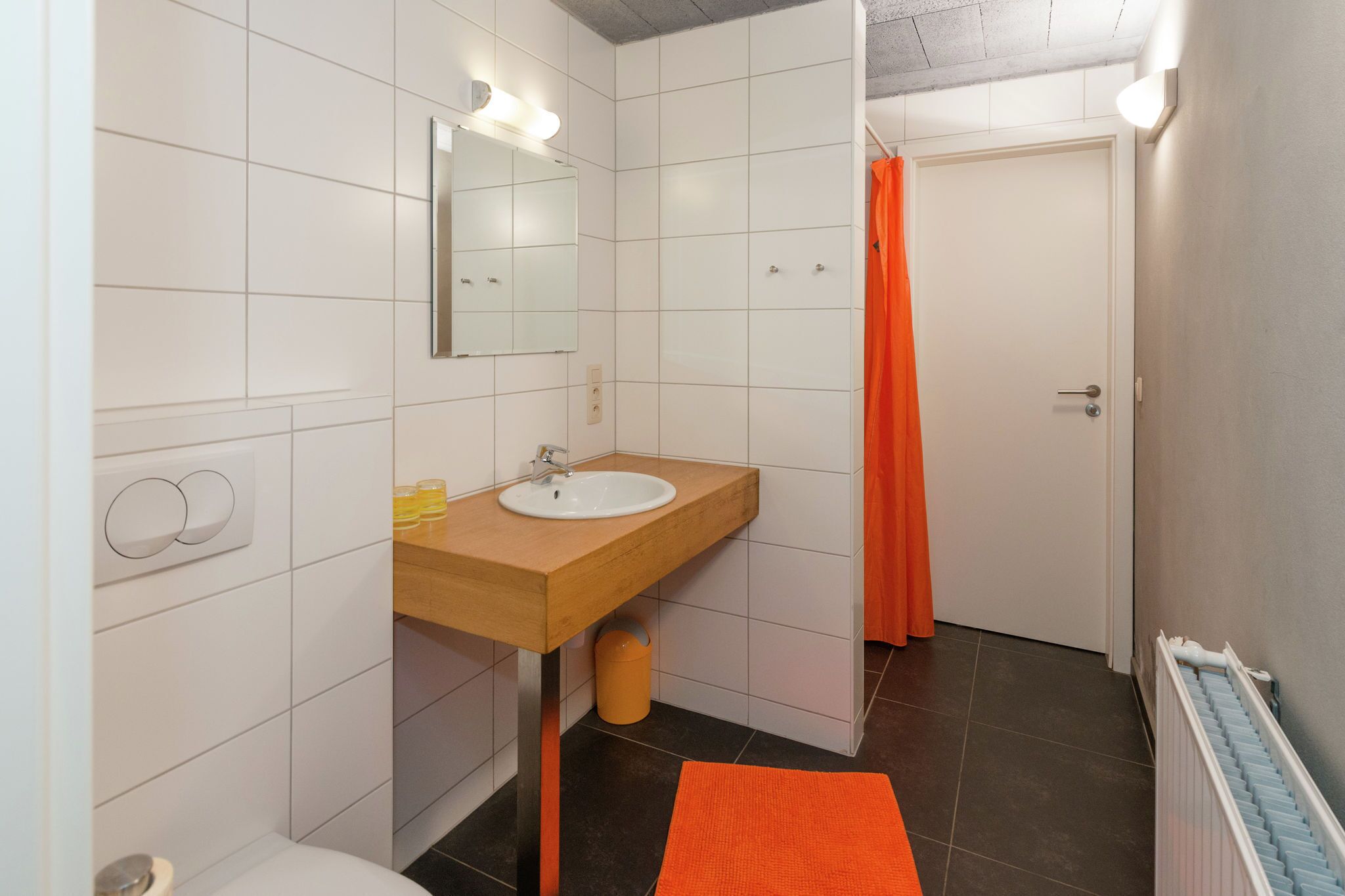 A bathroom with a white sink, mirror, and orange shower curtain.
