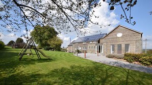 Un bâtiment doté d’un toit en pente, de panneaux solaires et d’une pelouse bien entretenue avec une balançoire.