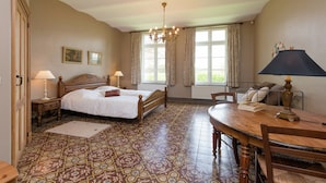 A bedroom with a large bed, two bedside tables with lamps, a wooden dining table, and a chandelier. - Le Hameau du Château – Elegance and serenity (Libin)